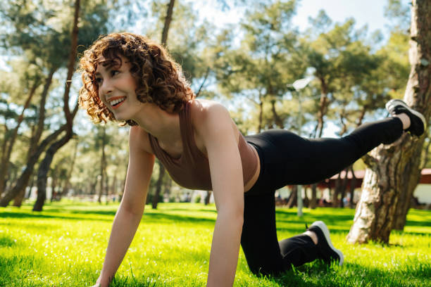 Young redhead happy fitness woman practicing yoga doing bird dog exercise on a city park, outdoors. stock photo