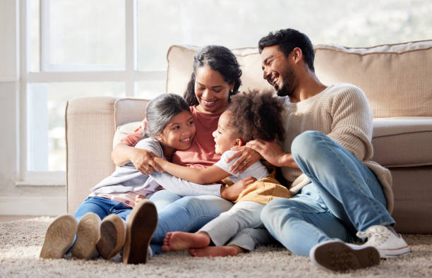 Affectionate and loving mixed race family sitting together. Happy family with two daughters hugging their mother and bonding at home. Two little girls enjoying a happy childhood with mom and dad stock photo