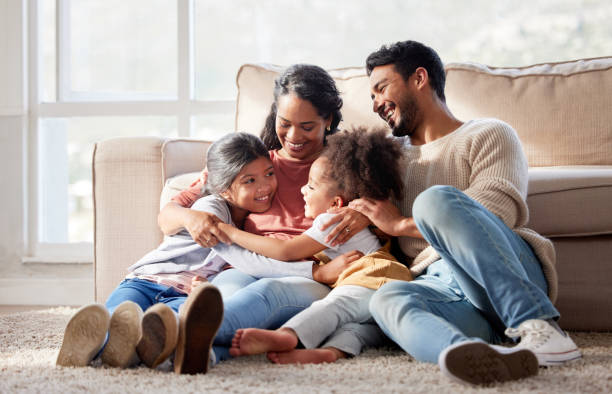 família mestiça carinhosa e amorosa sentada juntas. família feliz com duas filhas abraçando a mãe e se unindo em casa. duas garotinhas curtindo uma infância feliz com a mãe e o pai - child family offspring fun - fotografias e filmes do acervo