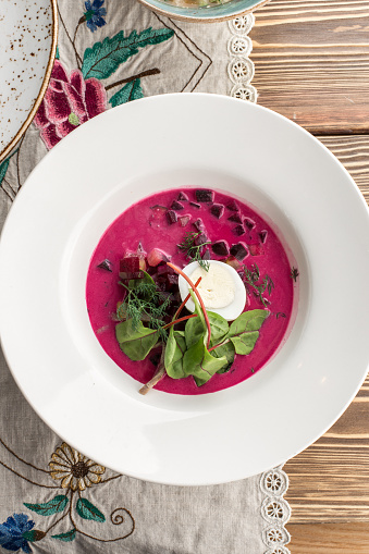 Beet cream cold soup with garlic and sour cream on white plate on wooden table top view