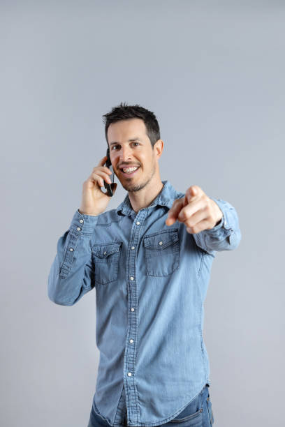 istock Smiling Man talking on phone in studio shot, looking and pointing at camera. 1398070377