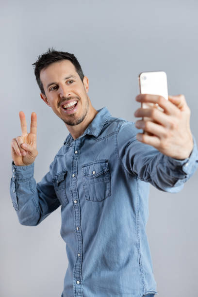 istock Man doing selfie shot on mobile phone, showing victory sign. 1398070411