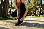 Female sport fitness runner getting ready for jogging outdoors on way. Running shoes - closeup of woman wearing sports bra and black legging tying shoe laces.