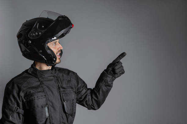 istock Man wearing protective black motorcycling equipment, pointing a side, indoors. 1398070647