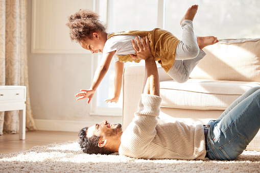 Father lifting daughter in the air. Excited girl playing with her dad. Young parent playing with their child. Happy dad lying on the floor having fun with daughter.