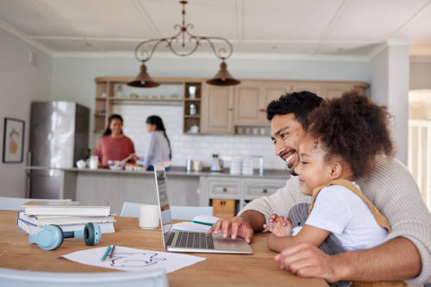 istock Happy young mixed race father and daughter using a laptop while sitting at a table together in the lounge at home. Hispanic dad and child looking at a laptop screen. Little girl bonding with her dad 1398070987