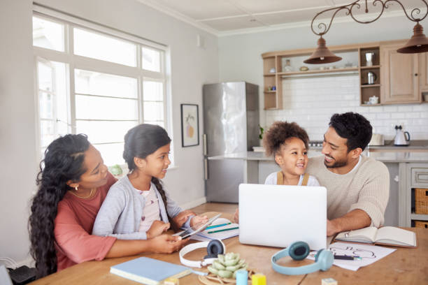 mixed race family using information technology at home. two little girls doing homework in the kitchen with help from their mother and father. parents and children working on school work together - child computer laptop little girls imagens e fotografias de stock