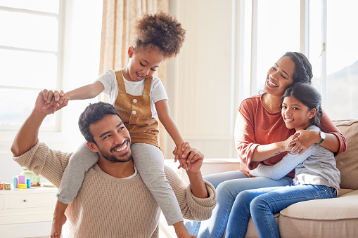 Happy mixed race family smiling while playing in the lounge together. Young hispanic couple spending quality time with their two cute little girls at home in a bright lounge