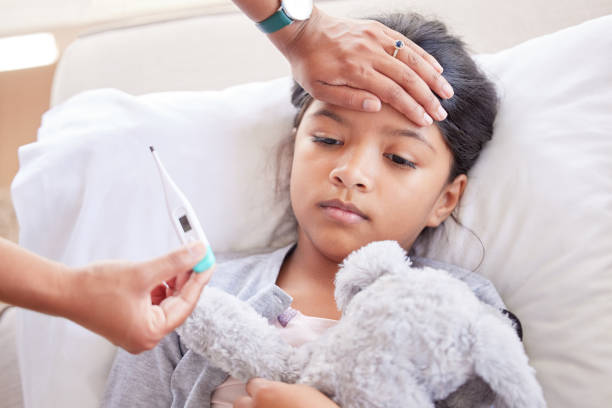 little girl having her temperature taken with a thermometer by her mother at home. small sick child lying in bed holding her toy, while a doctor checks her temperature. hispanic girl sick in hospital - child fever illness thermometer imagens e fotografias de stock