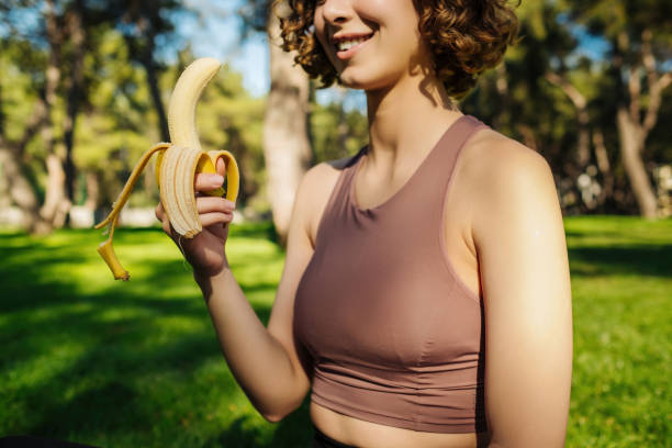 Young redhead fitness woman wearing sports bra training outdoors eating healthy banana for strength and energy. Outdoor sport concepts. stock photo