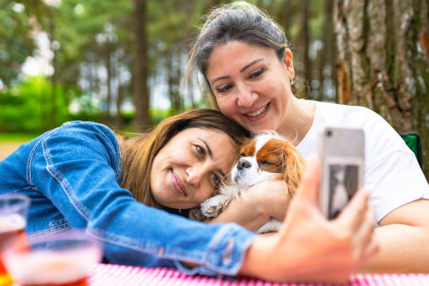 Same-sex couple picnicking and taking pictures with their dog stock photo