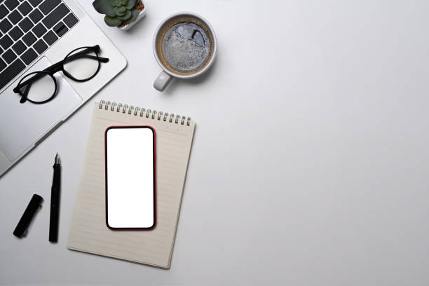 istock Top view mobile phone, laptop, notebook, glasses and coffee cup on white table. Minimal workplace, copy space. 1398075349