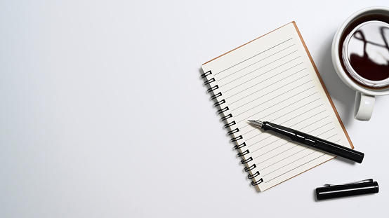 Notebook, coffee cup and pen on white background. Top view with copy space.