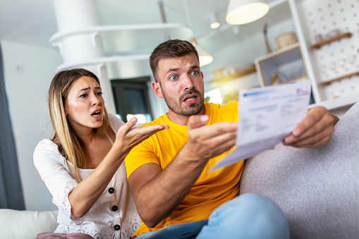 Worried couple checking bank account trouble sitting on a couch in the living room at home