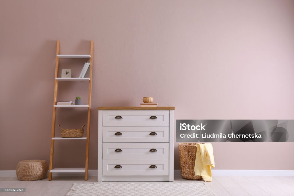 Elegant room interior with stylish chest of drawers, shelving unit and wicker basket. Space for text Storage Compartment Stock Photo