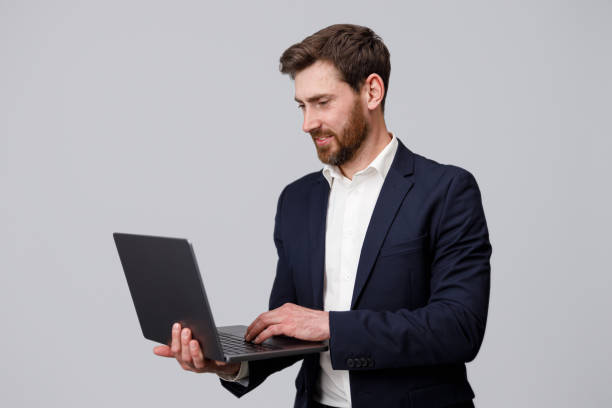 istock Handsome man in suit working online on laptop over grey studio background 1398076608