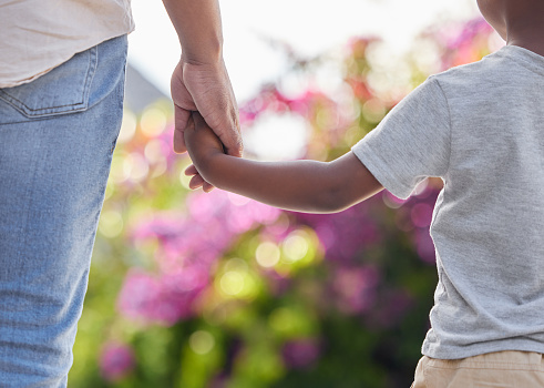 Closeup father and son holding hands while walking outside in the garden. A great role model and mentor for his boy child. A son will always look up to and follow in their dad's footsteps