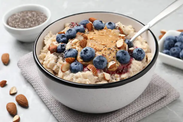 Tasty oatmeal porridge with toppings served on light grey table