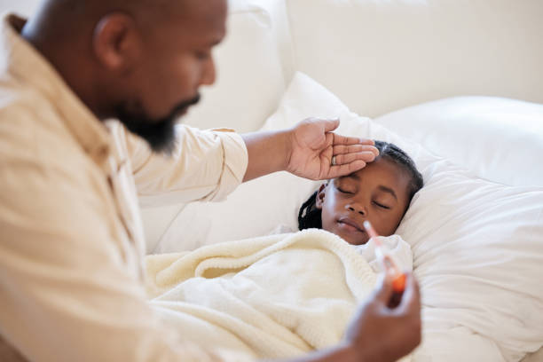 istock African american father checking his sick daughters temperature while taking care of her at home. Little girl sleeping in bed while her dad checks her fever. Man feeling his daughters forehead 1398080263