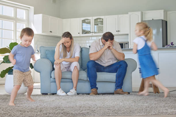 istock Tired and stressed parents suffering from a headache while adhd kids run around the living room. Noisy naughty siblings annoying their mother and father at home. Hyperactive and energetic children 1398087124