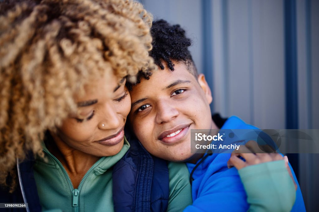 Portrait of a teenage son and mid adult mother embracing Portrait of a smiling mature woman and her fifteen years old boy, embracing and kissing Teenager Stock Photo