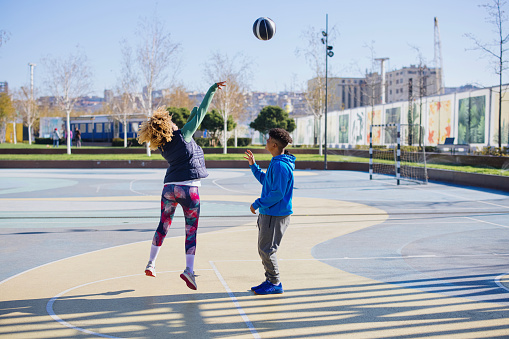 Mother and teenage son play basketball on an outdoor court