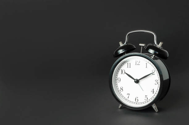 istock Black vintage alarm clock with white dial on black background flat lay copy space. Retro clock, mechanical alarm clock. Minimalistic background, concept of time, deadline, time to work, morning 1398090398