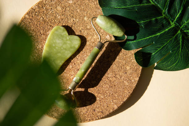 istock Jade Gua sha scraper and face roller massager on a cork round stand with a monstera leaf. 1398090521