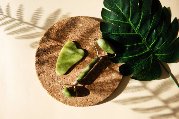 istock Jade Gua sha scraper and face roller massager on a cork round stand with a monstera leaf. 1398090721