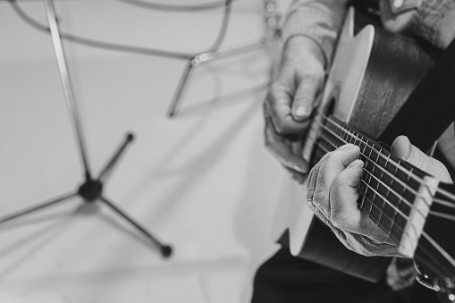 Focus on guitar neck. Close-up hands and acoustic guitar. Cropped monochrome portrait of man, rock musician playing guitar isolated on light background. Concept of art, music, style, details.