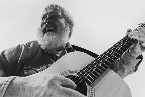 Looks happy, astonished. Bottom view of emotional senior bearded man, musician playing guitar isolated on white background. Concept of art, music, style, older generation, vintage, retro. Monochrome