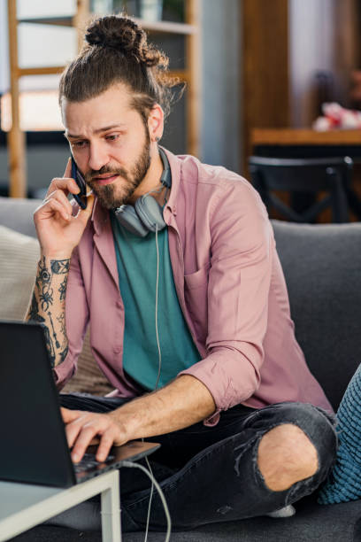 istock Handsome young hipster man working on a laptop computer at home, using a smartphone. 1398093485