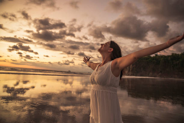 istock Lady's silhouette with raised arms against calm sunset beach 1398096979
