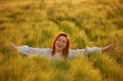 Redhead woman with toothy smile enjoying carefree time in nature on a wheat field in the sun