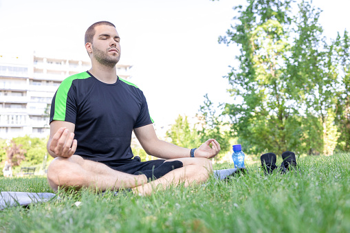 Fit young man doing meditation exercises at the park
