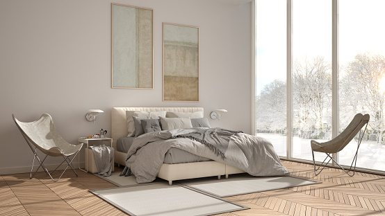 Modern white minimalist bedroom, double bed with pillows and blankets, parquet, bedside tables and carpet. Panoramic window with winter panorama with trees and snow, interior design