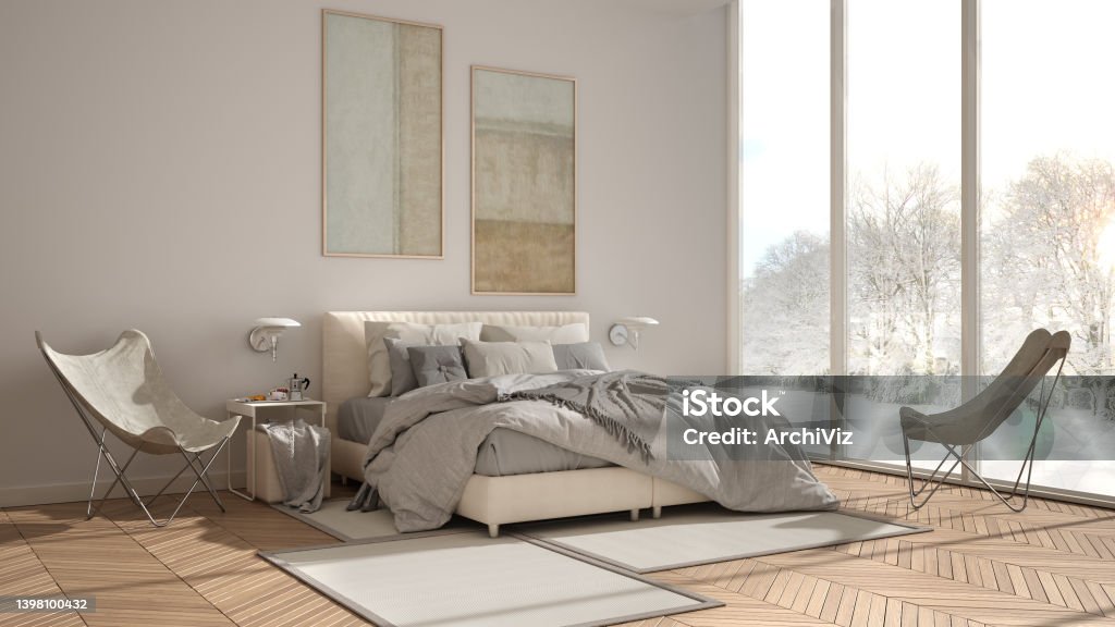 Modern white minimalist bedroom, double bed with pillows and blankets, parquet, bedside tables and carpet. Panoramic window with winter panorama with trees and snow, interior design Flooring Stock Photo