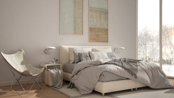 istock Modern white minimalist bedroom, double bed with pillows and blankets, parquet, bedside tables and carpet. Panoramic window with winter panorama with trees and snow, interior design 1398100438