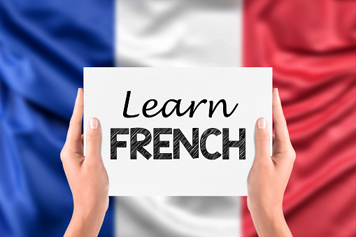 French learning concept. Learn french written on a paper card in hands with blurred France flag background