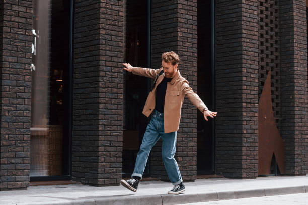 istock Having fun by walking the sidewalk. Stylish man with beard in khaki colored jacket and in jeans is outdoors near building 1398103982