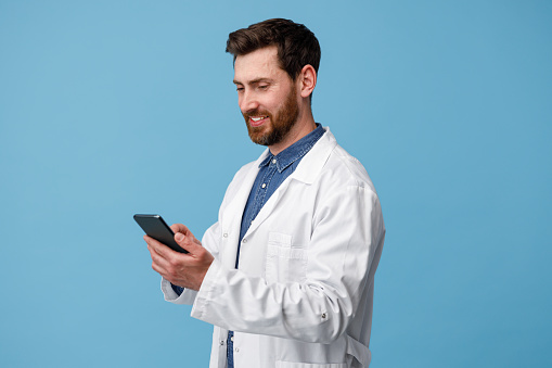Man Doctor using mobile phone over blue studio background. Healthcare and medical concept