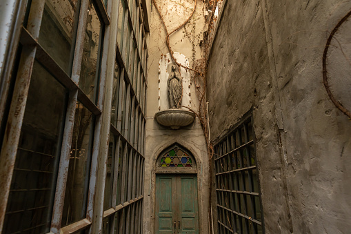 front view of narrow alley entrance of ancient church with old wooden door and stone woman statue