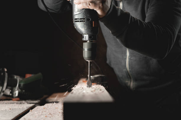 istock A man works with a drill in his workshop. Carpenter drills with a hand power tool in a dark room with directional light 1398106853
