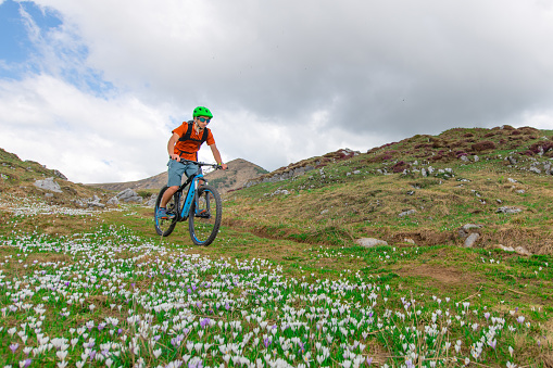 A young mountain biker rides down a mountain meadow in spring among flowers