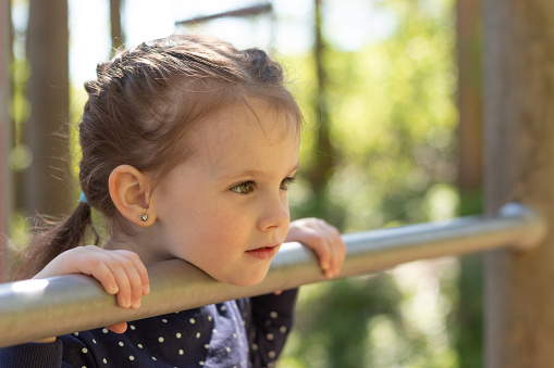 Little beautiful girl with braided pigtails has fun on the uneven bars in the park