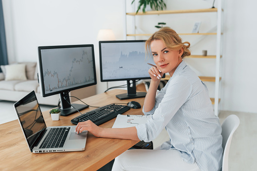 Side view. Female stock broker in formal wear is working in the office. TradingView on screen