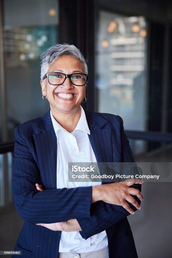 Smiling mature businesswoman standing in the hallway of an office Portrait of a smiling mature businesswoman standing with her arms crossed in an office building corridor Businesswoman Stock Photo