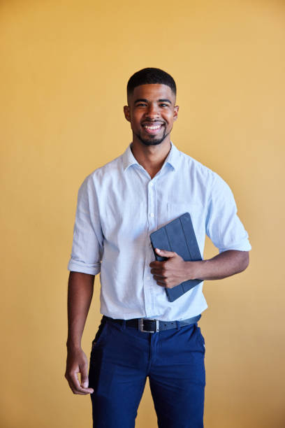 istock Smiling young businessman holding a tablet against a yellow background 1398114637