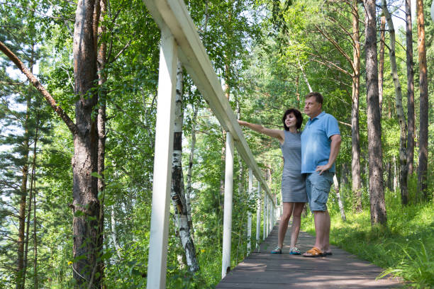 une femme brune parle avec enthousiasme de quelque chose à un homme pointant du côté dans un parc verdoyant - short tall men couple photos et images de collection