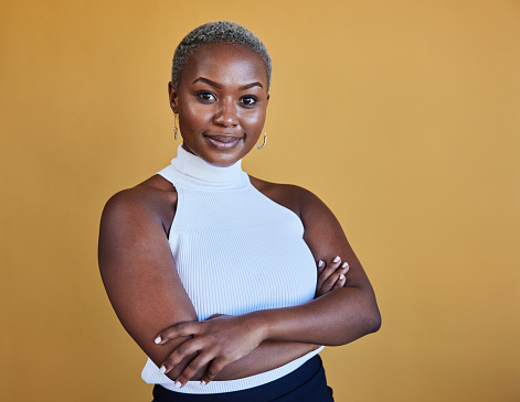 Portrait of a confident young African businesswoman with short hair standing with her arms crossed in front of a yellow background